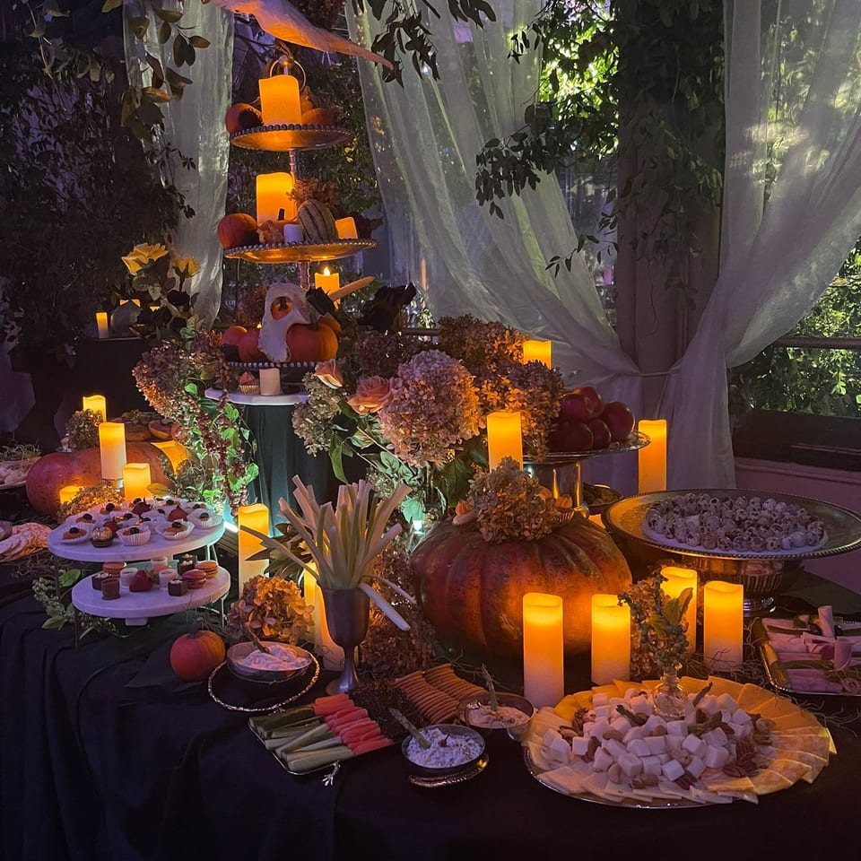 A dimly lit Halloween-themed buffet table with pumpkins, candles, desserts, and snacks.