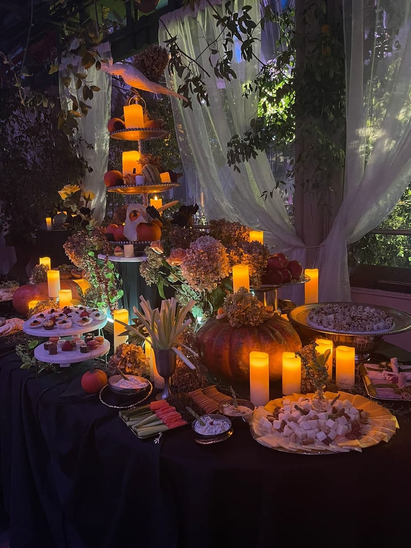 A dimly lit Halloween-themed buffet table with pumpkins, candles, desserts, and snacks.
