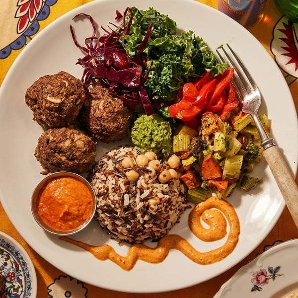 A colorful vegan plate with falafel, rice, vegetables, and sauces on a patterned yellow tablecloth.